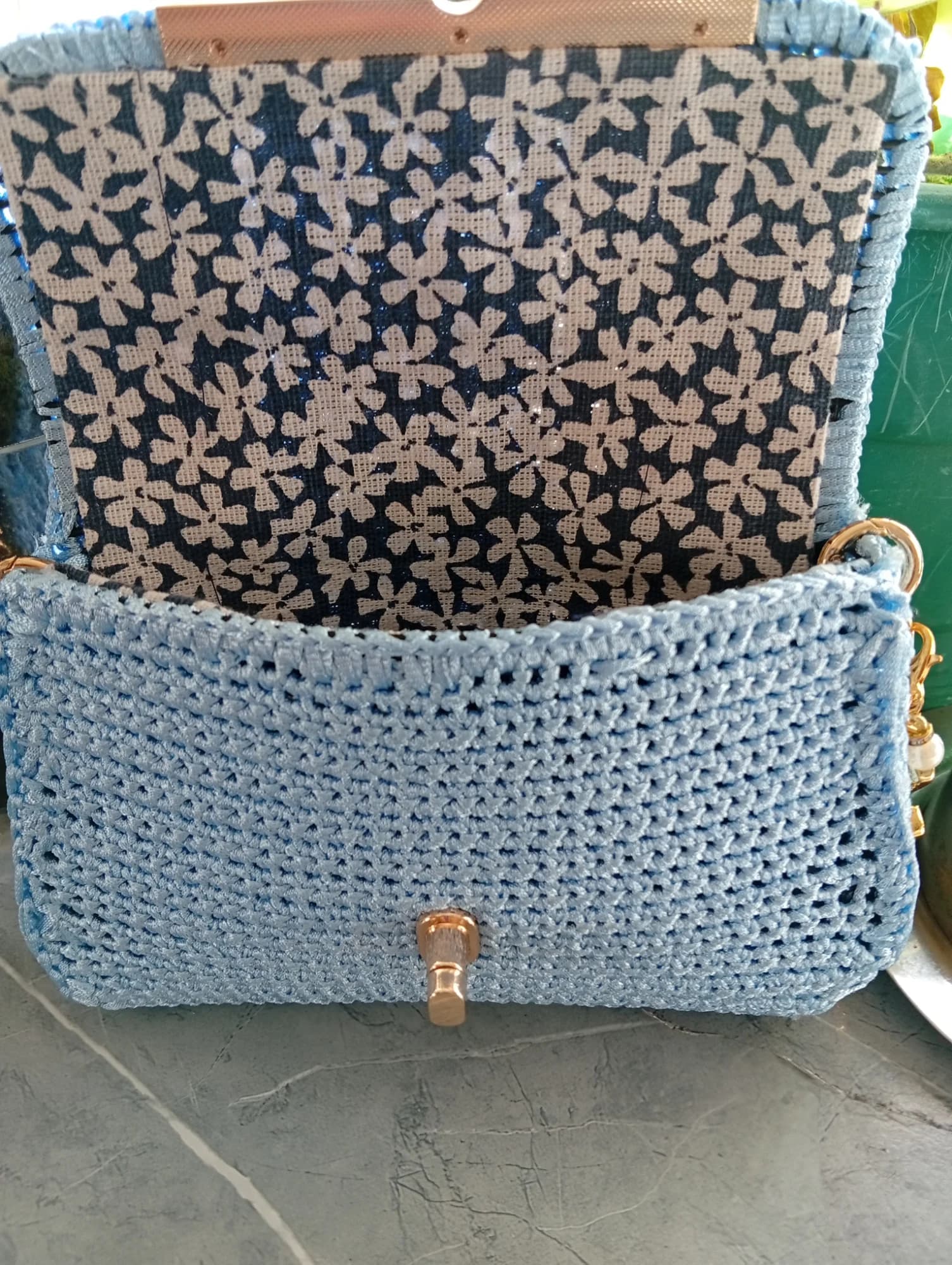 Carteira de croché azul-claro aberta, com forro floral escuro e aba de fecho visível.