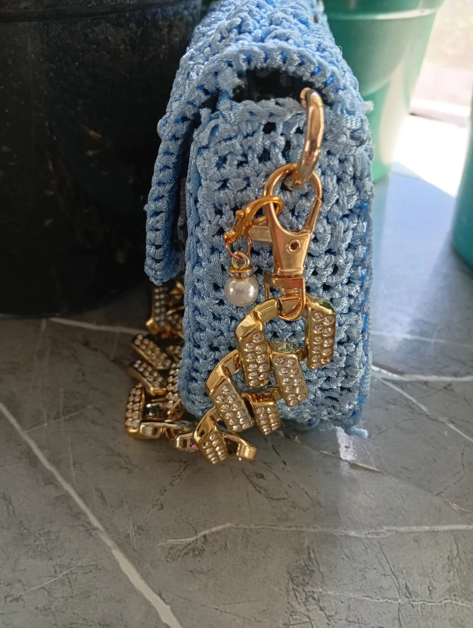 Clutch azul em croché vista de lado, com argola e pendente dourado.