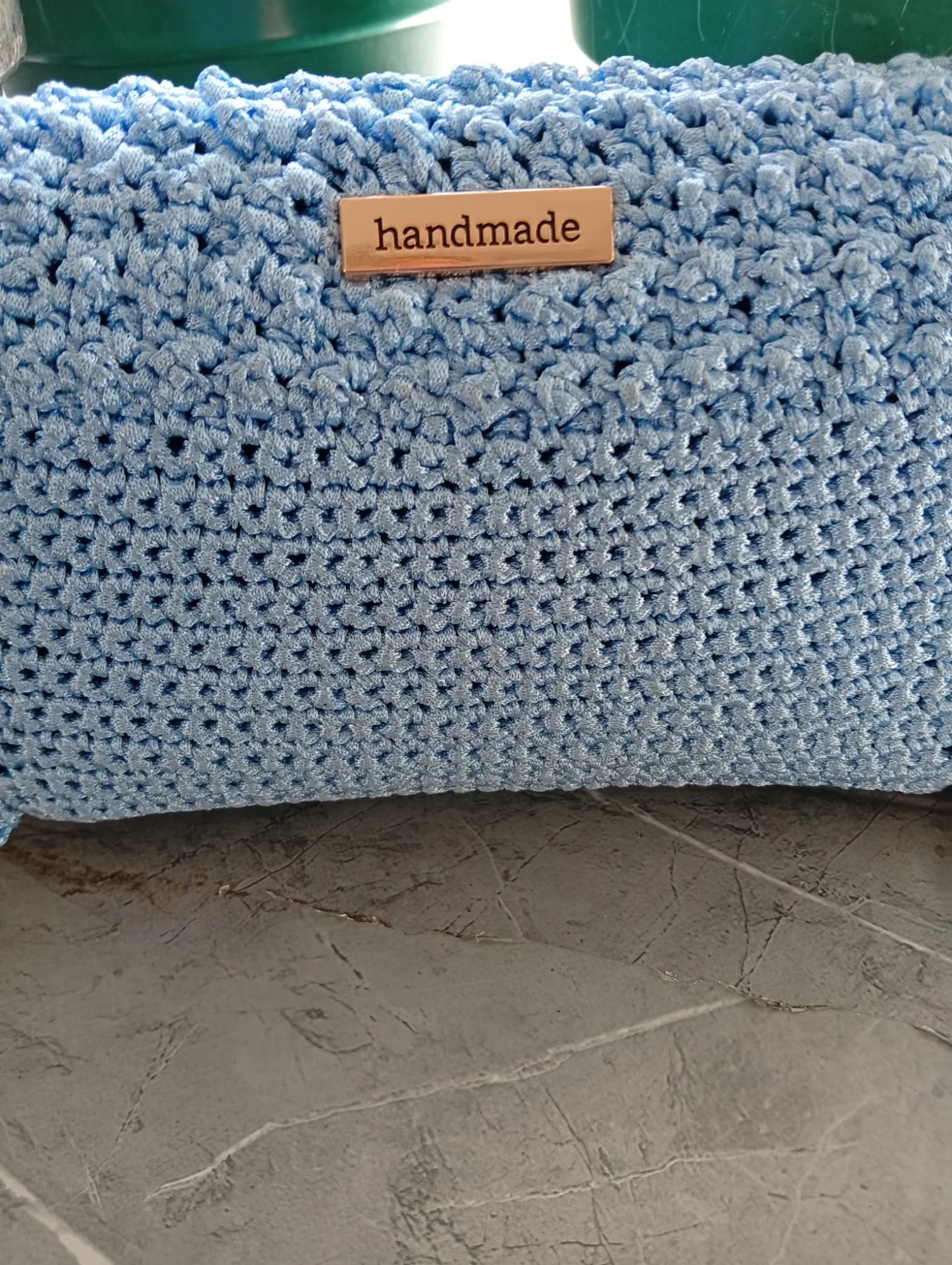 Mala em croché azul-claro com placa metálica dourada a dizer handmade.
