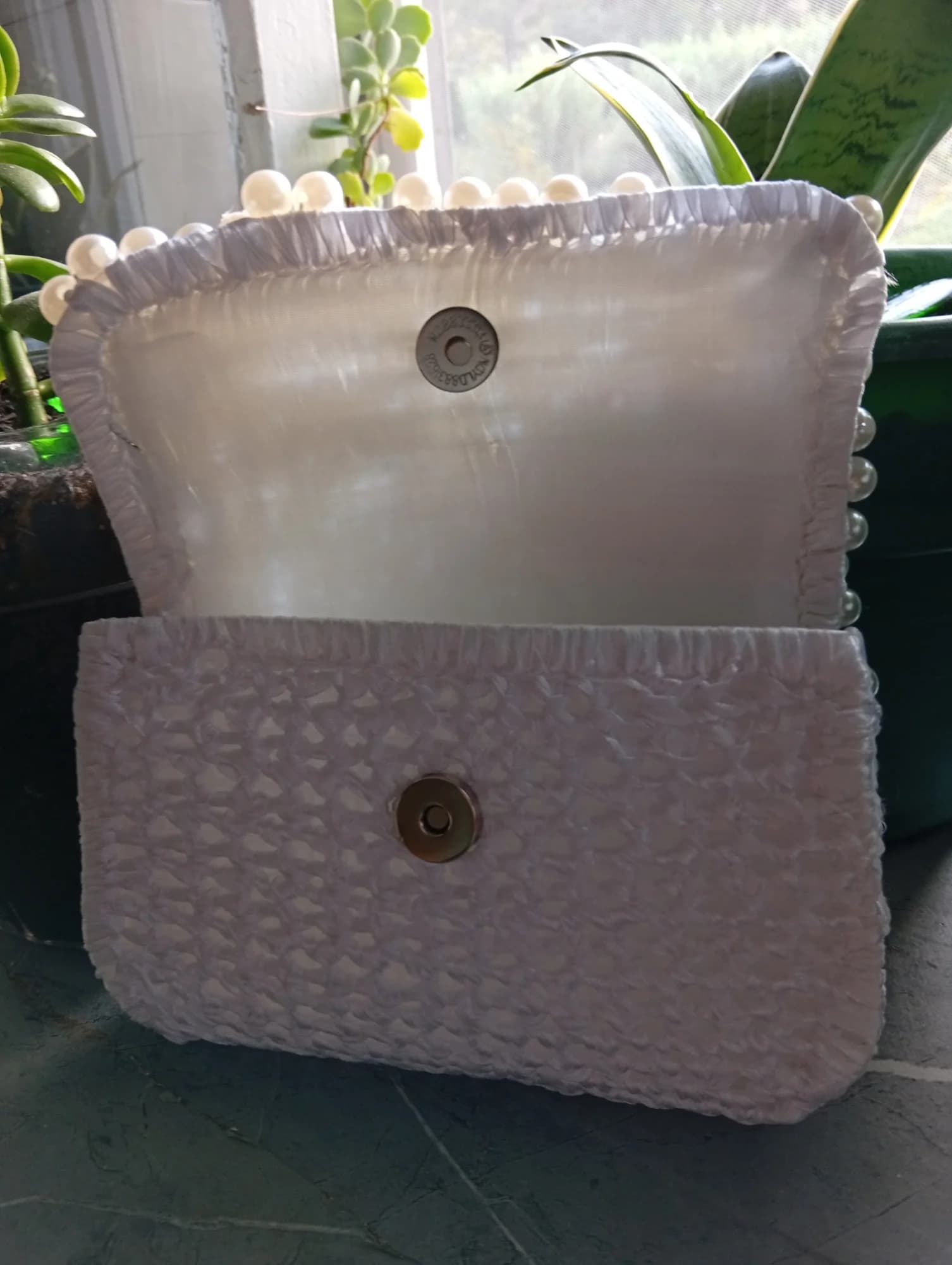 Bolsa em croché branco com aba lisa e fecho metálico, vista de trás.